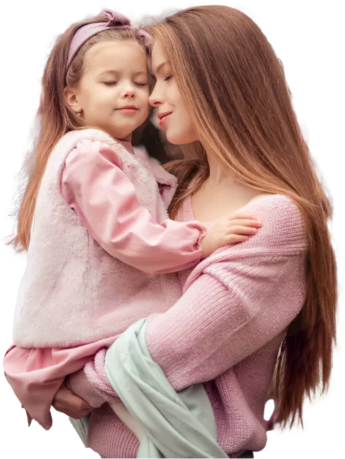 A woman in a pink sweater tenderly holding a young girl in a pink dress and headband, both with eyes closed.